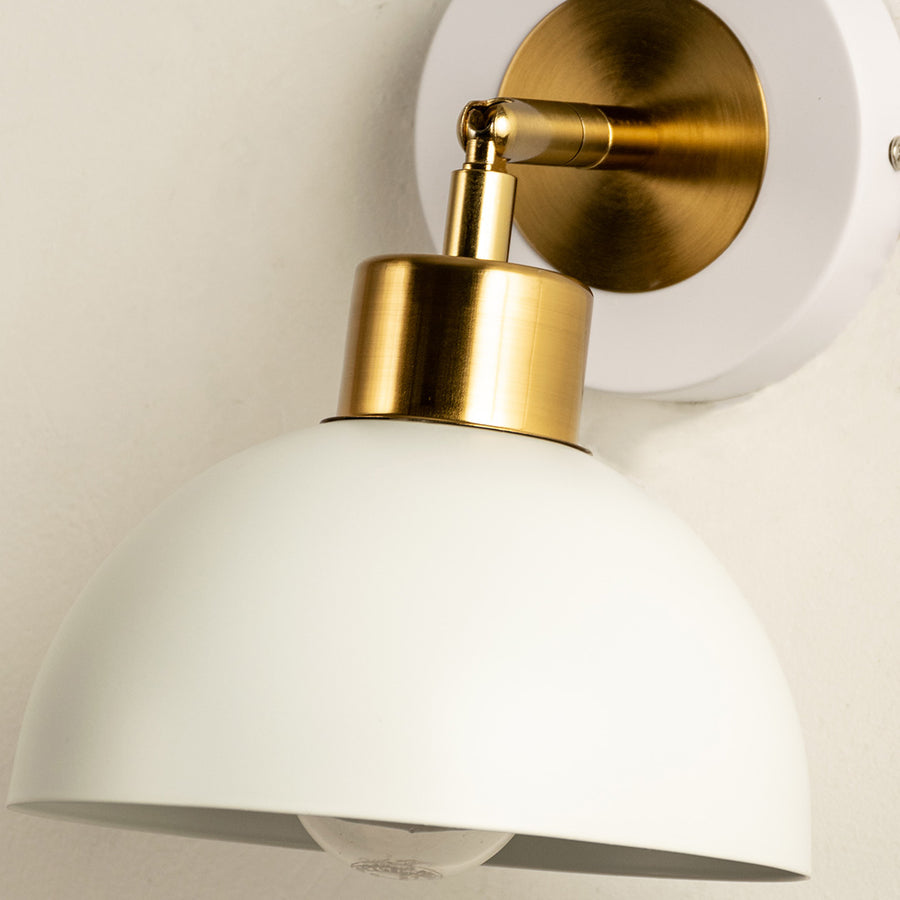 Closeup of wall light with white metal dome shade and gold holder showcasing smooth finish and modern interior decor styling.
