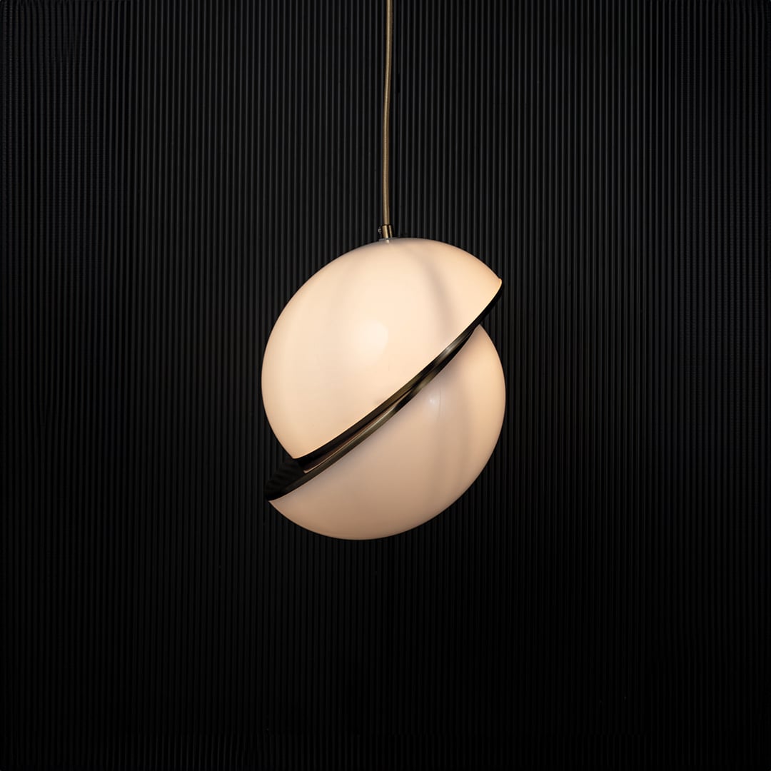 A modern spherical pendant light glowing warmly against a dark black backdrop highlighting the gold detailing and soft ambient shine created when the light is on.