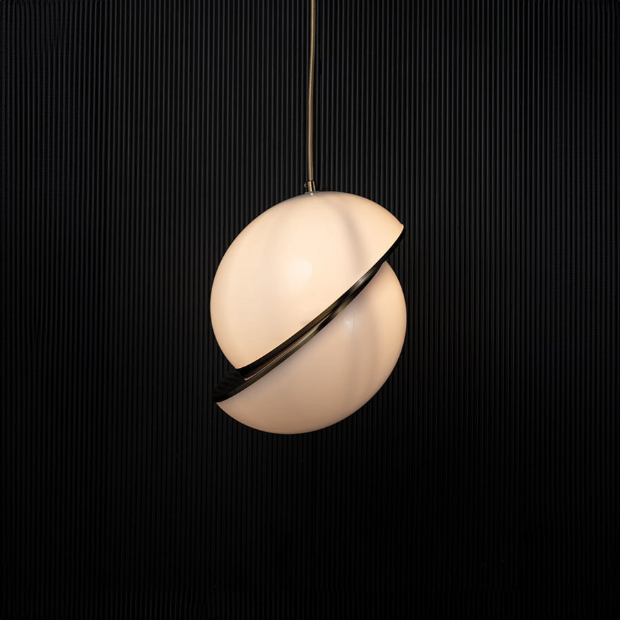 A modern spherical pendant light glowing warmly against a dark black backdrop highlighting the gold detailing and soft ambient shine created when the light is on.
