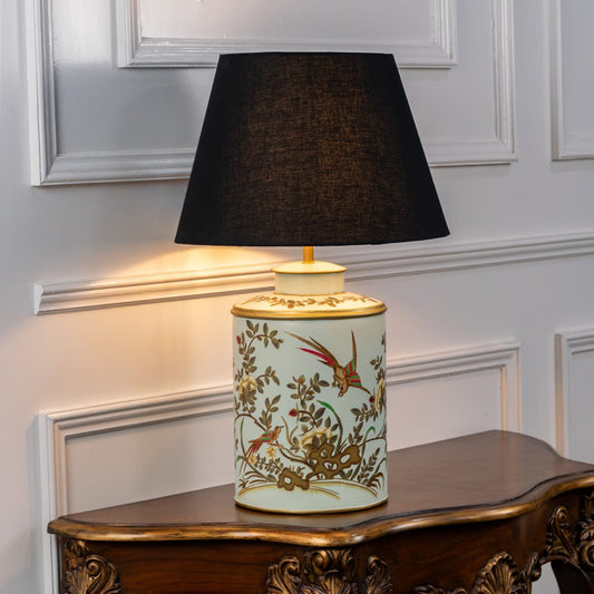 Table lamp with floral ceramic base and black fabric lampshade placed on a wooden surface against a clean white background.