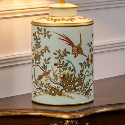Table lamp closeup showing hand painted bird and floral design on ceramic base with soft green background and gold rim.