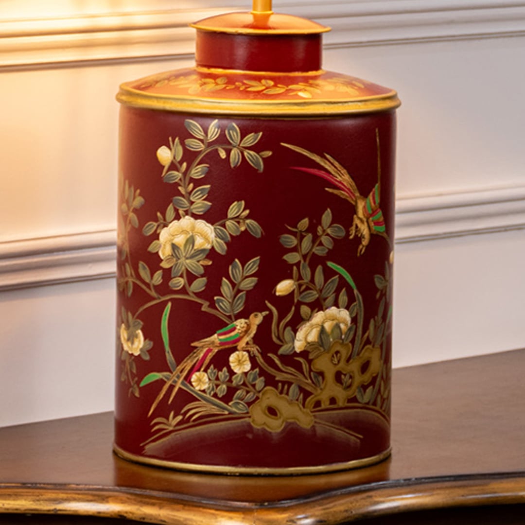 Closeup image highlights red ceramic lamp base with floral branches birds and gold rim detailing showing fine craftsmanship.