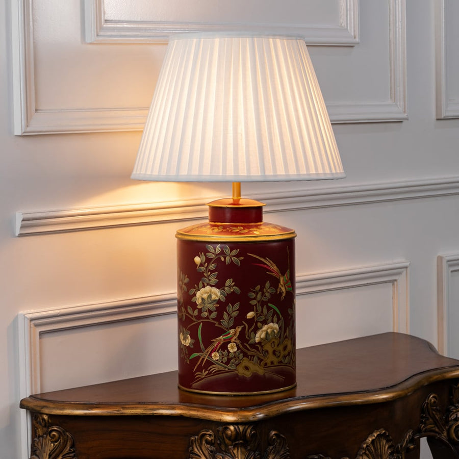 Light on white background features red ceramic table lamp illuminated to emphasize gold detailing floral motifs and warm light glow.