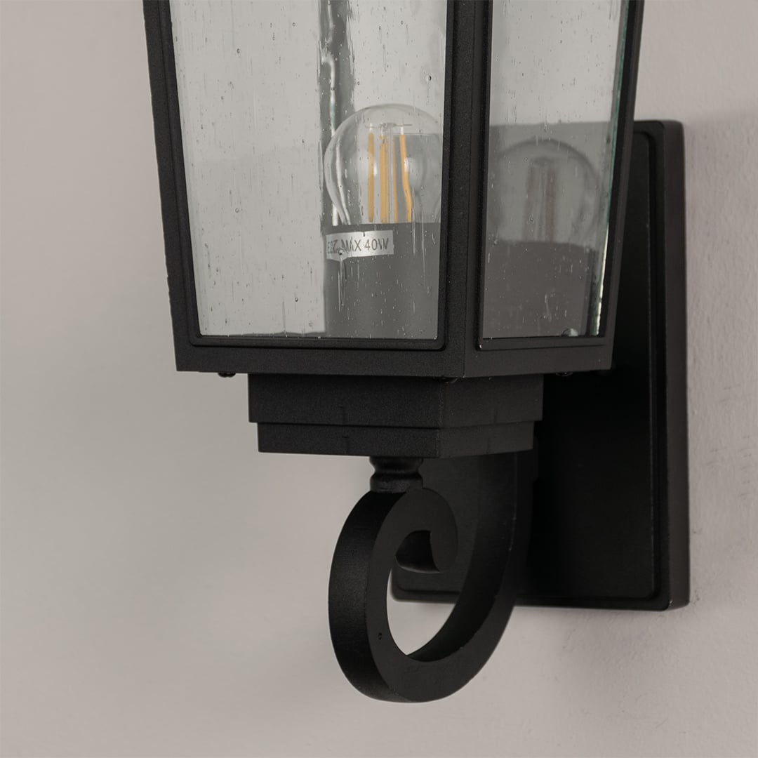 Closeup of black outdoor wall lantern showing detailed metal frame and clear textured glass for timeless exterior lighting.