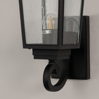 Closeup of black outdoor wall lantern showing detailed metal frame and clear textured glass for timeless exterior lighting.