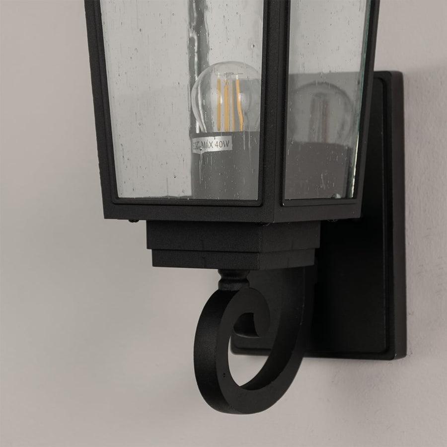 Closeup of black outdoor wall lantern showing detailed metal frame and clear textured glass for timeless exterior lighting.