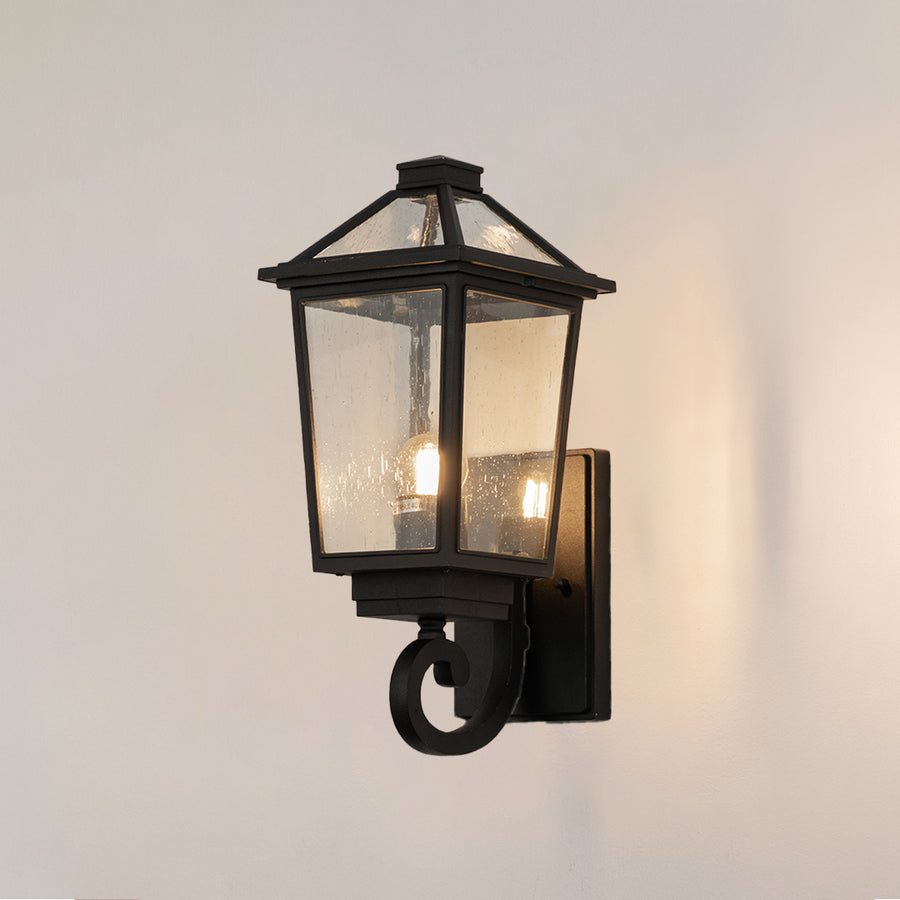 Black metal outdoor lantern wall light on white background with clear glass shade for classic exterior decor.