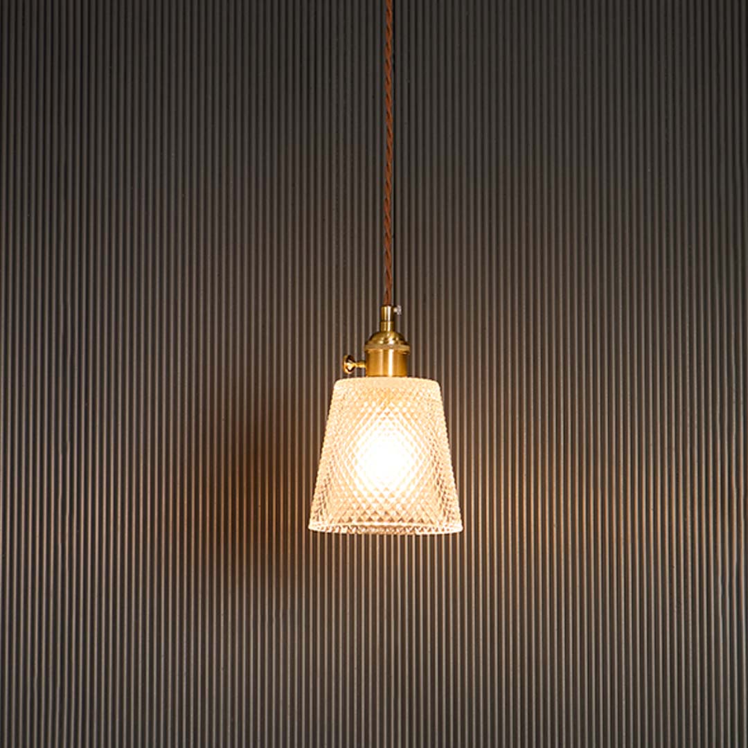 Clear textured glass pendant light with brass holder glowing warmly against black background for modern room ambience.