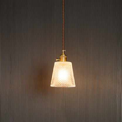 Clear textured glass pendant light with brass holder glowing warmly against black background for modern room ambience.