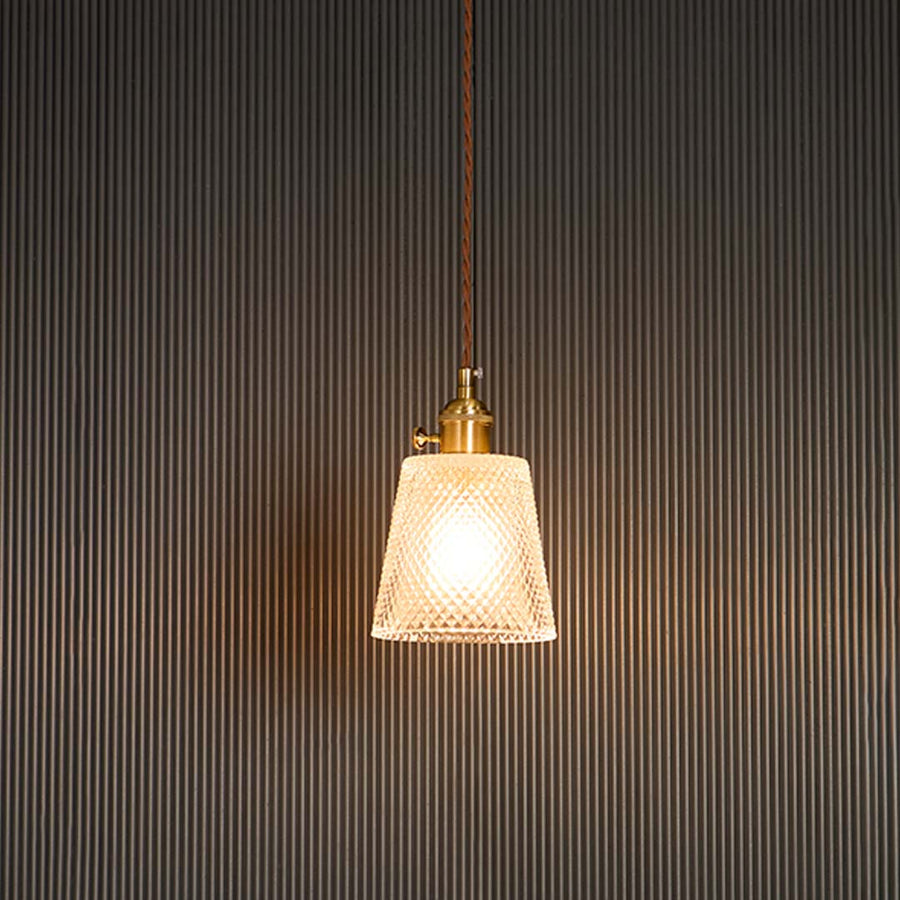 Clear textured glass pendant light with brass holder glowing warmly against black background for modern room ambience.