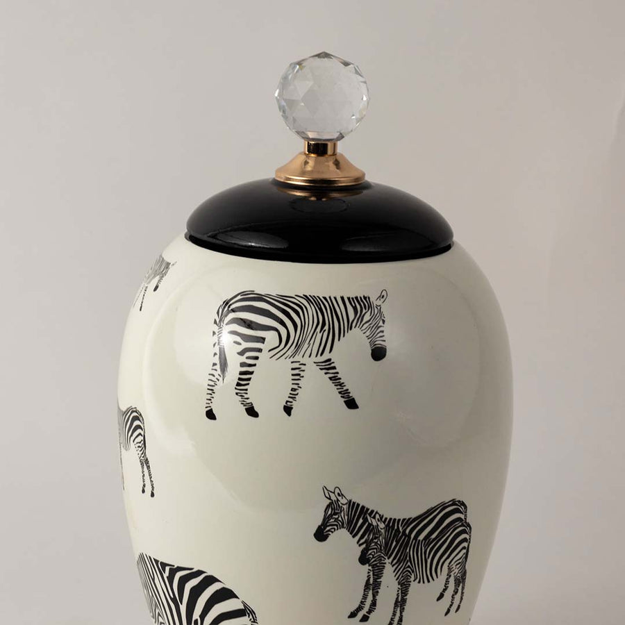 Closeup of white ceramic jar showing black zebra artwork and glossy finish with crystal knob and gold detailing.