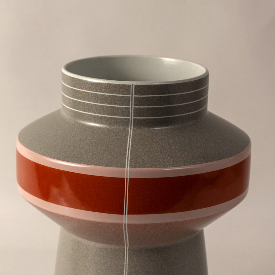 Modern ceramic vase with layered grey top and bold orange base placed on white surface against neutral background highlighting stylish geometric decor design.