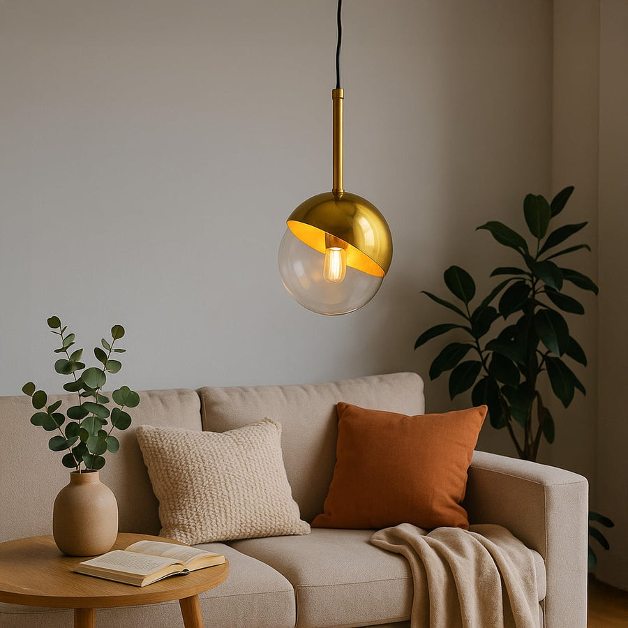 A modern gold and glass pendant light glowing warmly above a beige sofa in a cozy living room with plants and soft cushions creating a calm inviting ambiance.