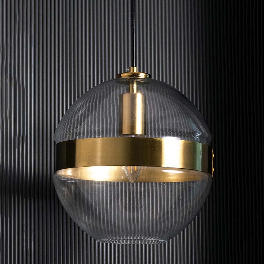 Round glass pendant with gold band shown against a dark ridged backdrop emphasizing its elegant shape and contemporary finish without light.