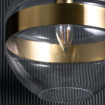 closeup of a modern glass pendant showing the gold band and clear spherical form with visible bulb elements creating a refined contemporary look.