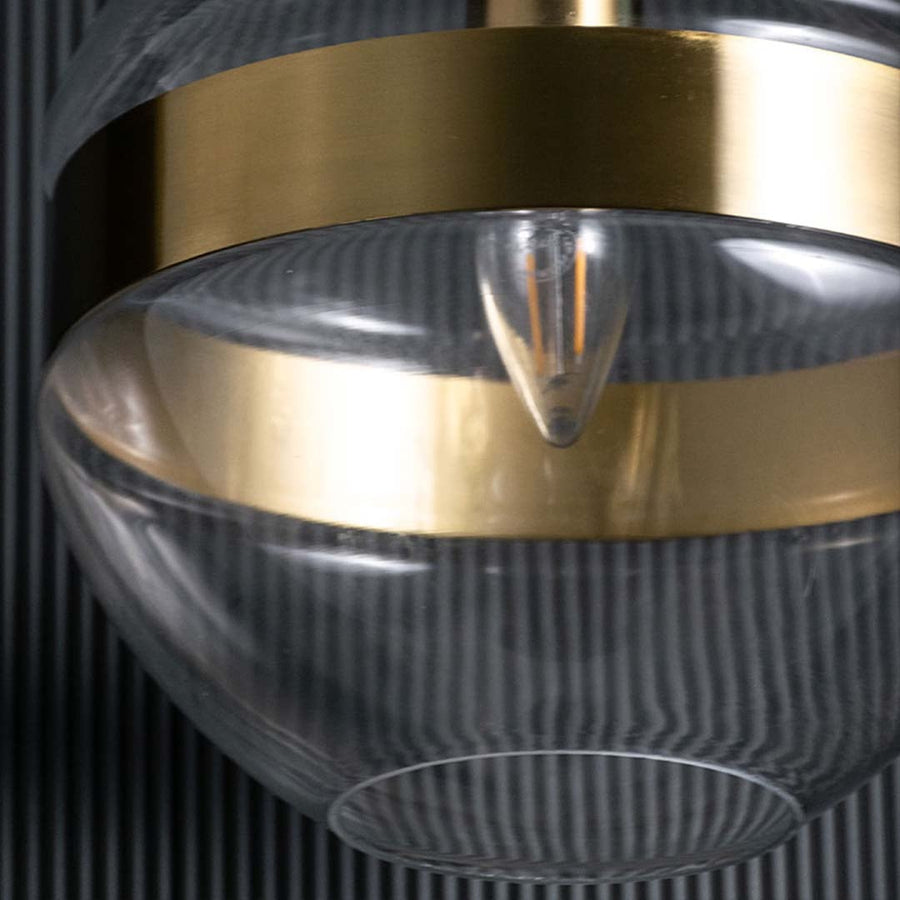 closeup of a modern glass pendant showing the gold band and clear spherical form with visible bulb elements creating a refined contemporary look.