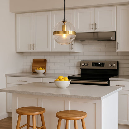 Modern round glass pendant light with gold band hanging over a bright white kitchen island with wooden stools and fresh lemons creating a warm contemporary look.