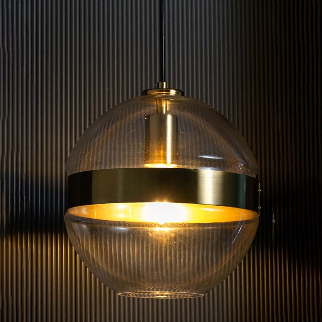 Glowing spherical pendant light with clear glass and gold detailing set against a dark textured background enhancing its warm ambient shine.