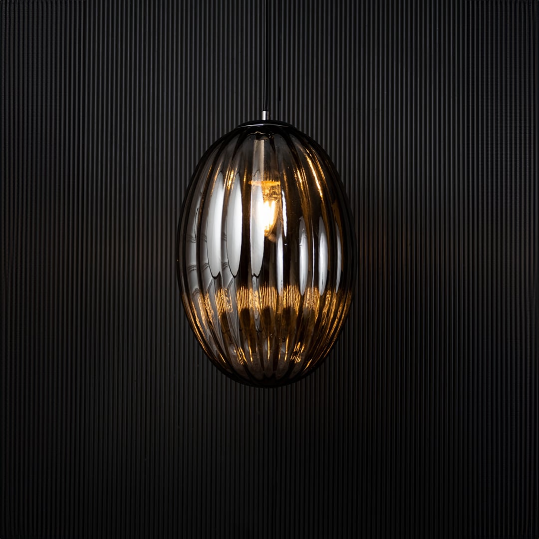 A ribbed oval glass pendant light shown with the light on against a dark background creating a soft glowing effect that enhances the elegant vertical contours.