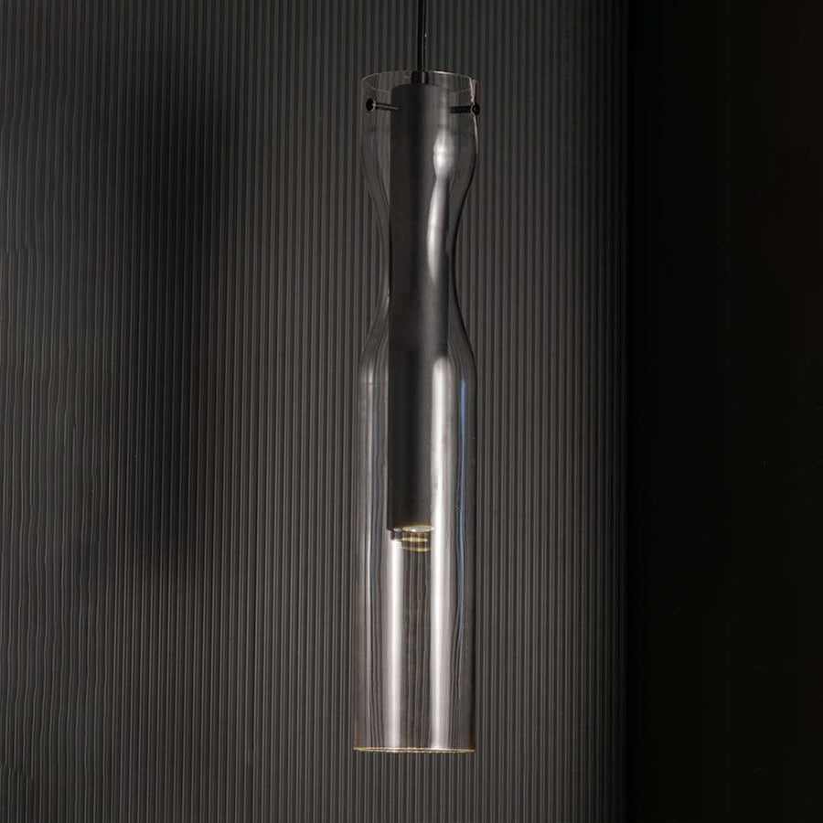 Slim black pendant light with a clear glass exterior shown against a black background highlighting its tall sculpted form with a sleek contemporary finish.