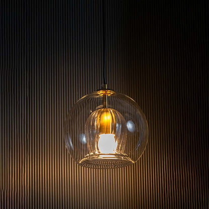 Glowing glass pendant with ribbed inner shade showcased on a black background creating a dramatic warm light effect around the elegant form.