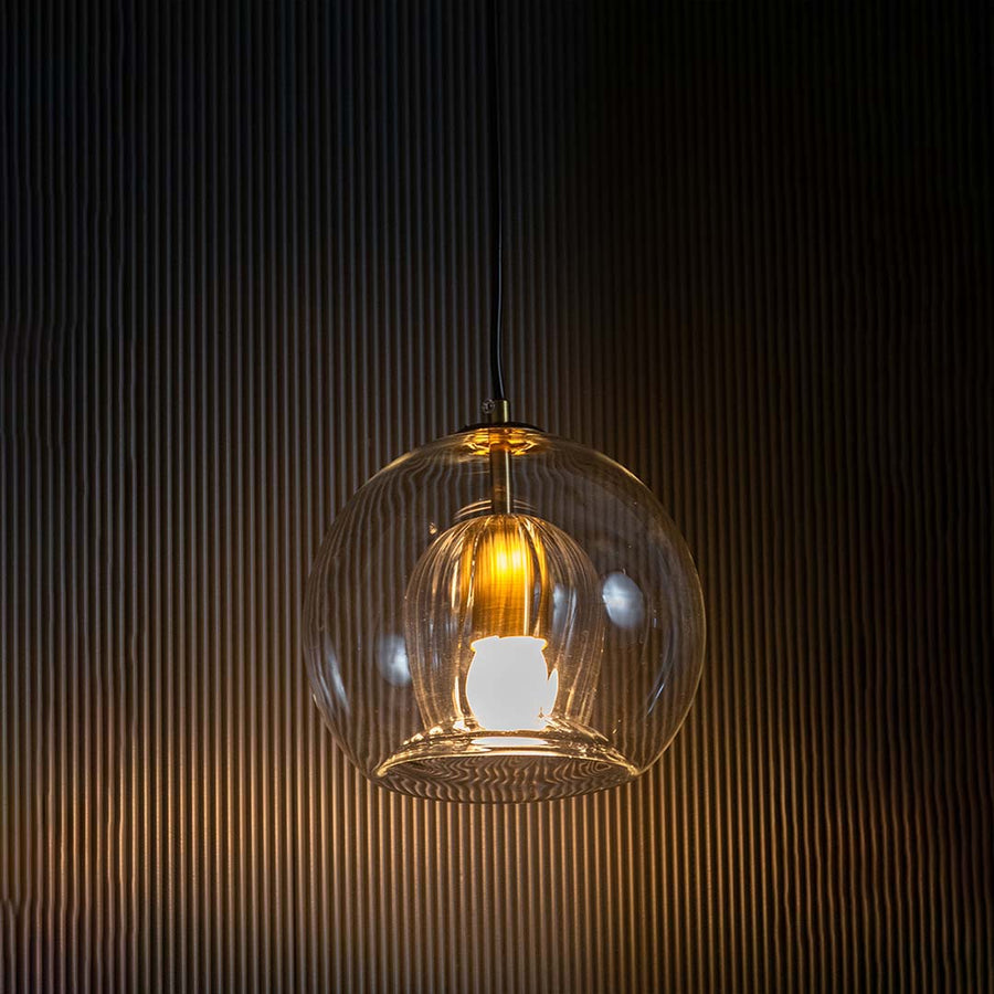 Glowing glass pendant with ribbed inner shade showcased on a black background creating a dramatic warm light effect around the elegant form.