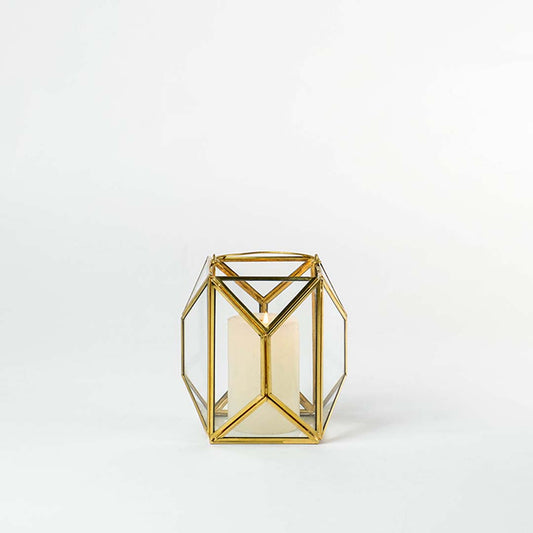 Gold metal and glass geometric lantern shown on a white background with candle on highlighting its modern structure and warm inviting glow.