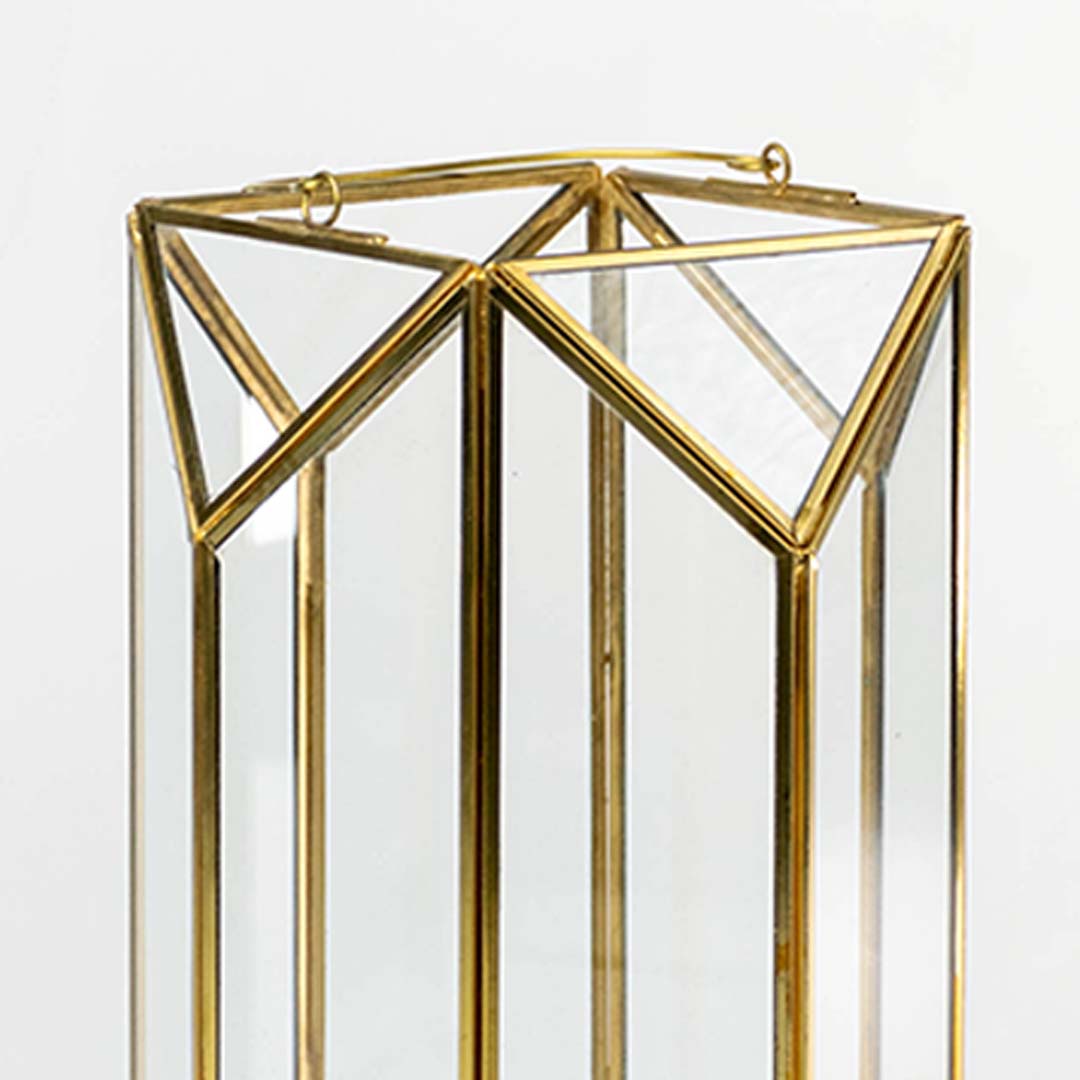 Closeup of gold metal and glass candle lantern showing geometric frame details and glossy glass panels creating a modern elegant decorative accent.