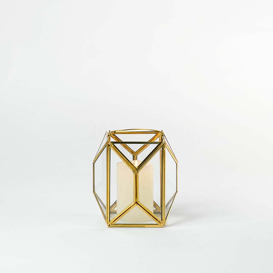 Gold metal and glass geometric lantern shown on a white background with candle on highlighting its modern structure and warm inviting glow.