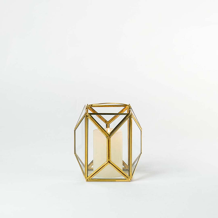 Gold metal and glass geometric lantern shown on a white background with candle on highlighting its modern structure and warm inviting glow.