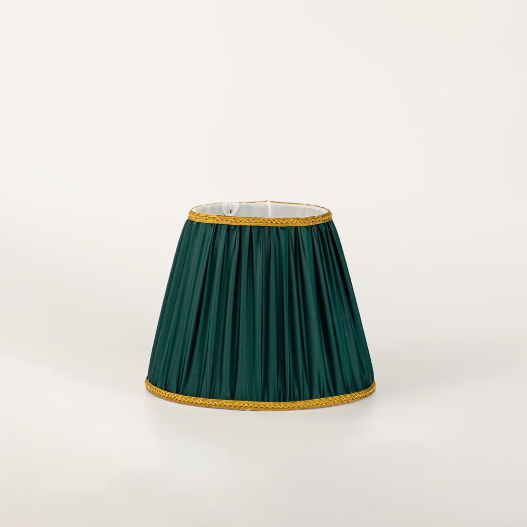 Pleated green lampshade with gold trim displayed on a light surface designed for classic table lamps and elegant home decor.
