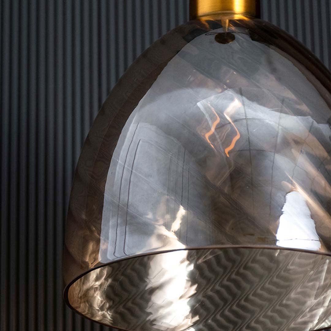 A closeup of the gold and smoked glass pendant light showing the swirled glass texture and metallic gold fitting ideal for premium interiors.
