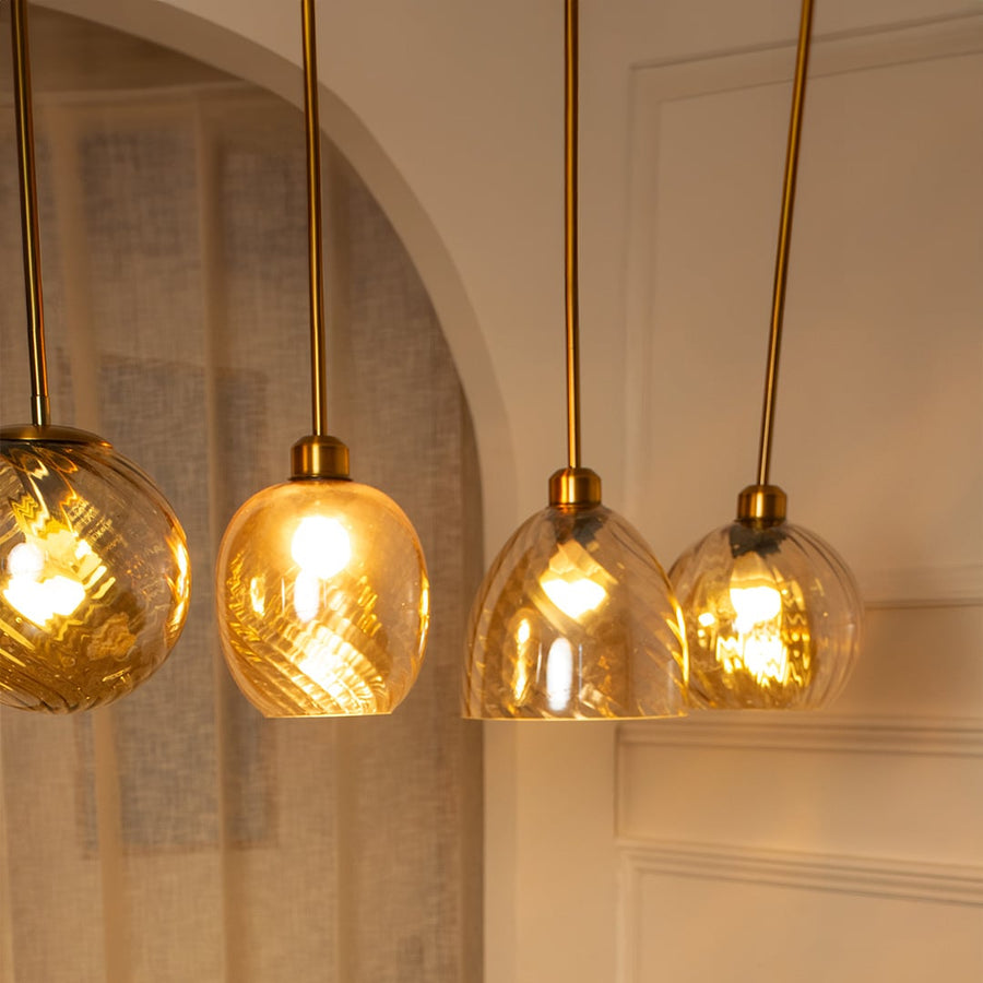 A grouped display of amber glass pendant lights with lights on creating warm ambient illumination perfect for dining areas and modern rooms.