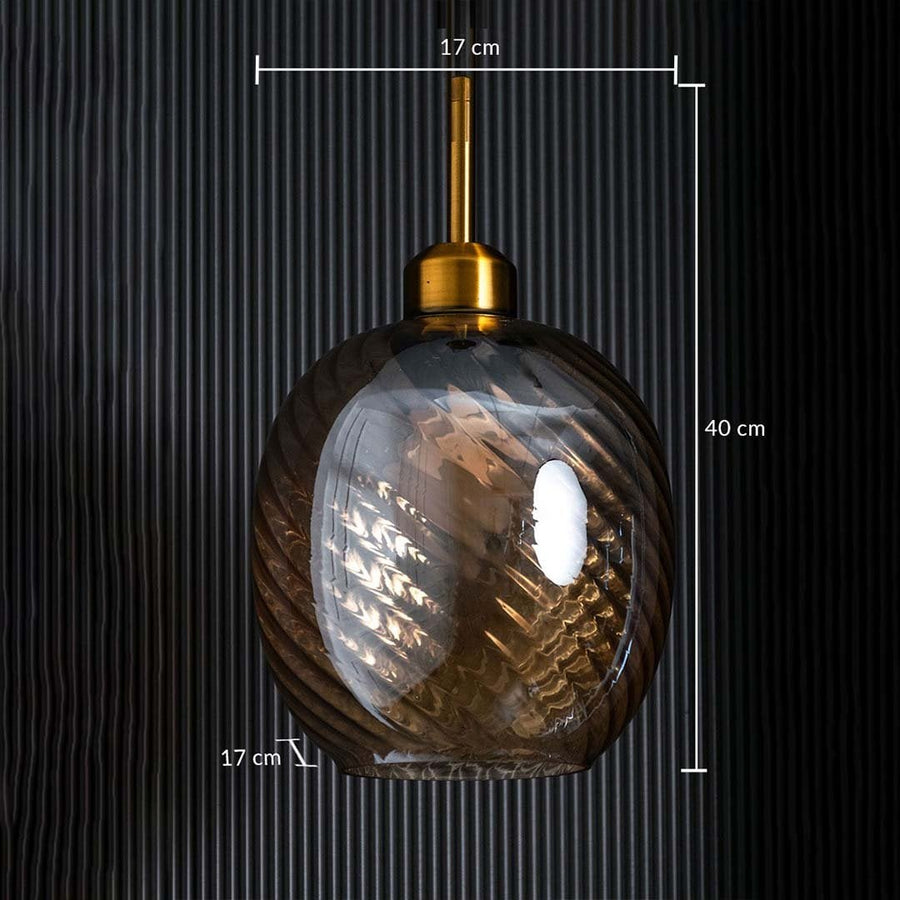 Glass and metal pendant light switched on showing a warm glowing bulb inside a clear spherical shade against a bright white background.