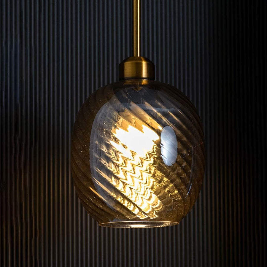 Glowing gold pendant fixture with textured glass shade set against dark background emphasizing intricate swirl patterns and warm ambiance.
