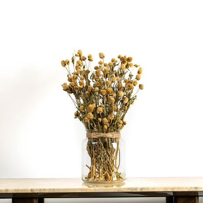Dried flower arrangement in a clear glass vase placed on a tabletop offering a rustic natural home décor look with warm golden tones ideal for enhancing cozy and earthy interior spaces.
