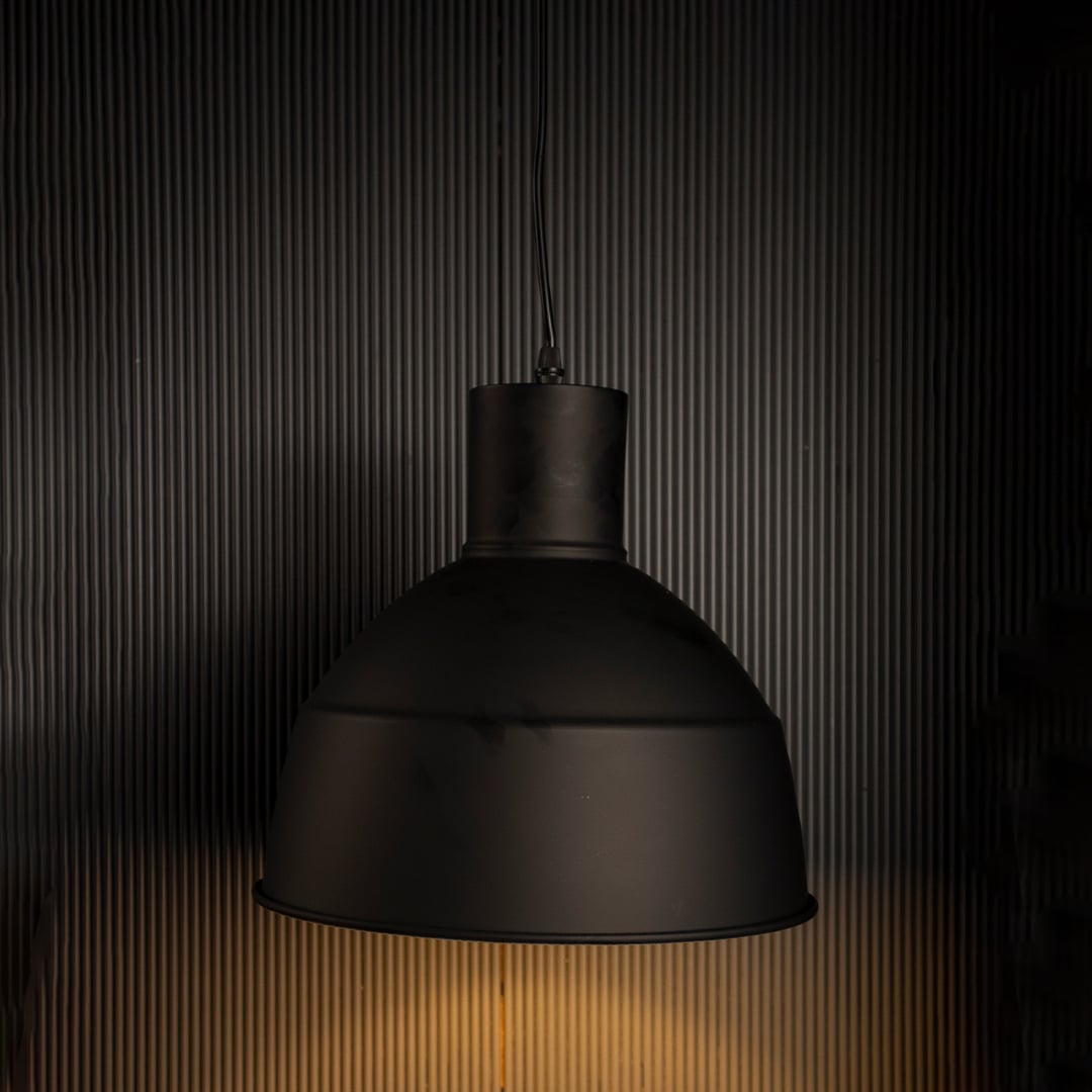 Illuminated black metal dome pendant lamp turned on suspended against a dark black background highlighting the rim shape.
