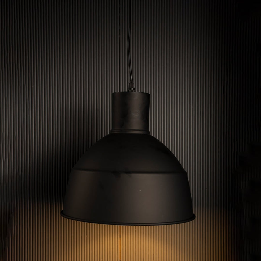 Illuminated black metal dome pendant lamp turned on suspended against a dark black background highlighting the rim shape.