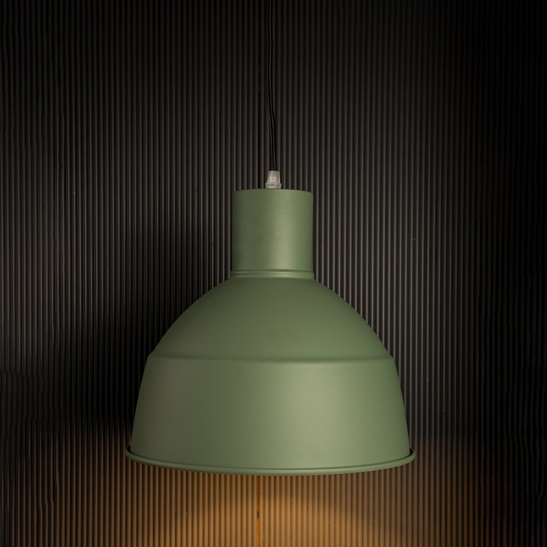 Illuminated green metal dome pendant lamp turned on suspended against a dark black background highlighting the rim shape and warm light.