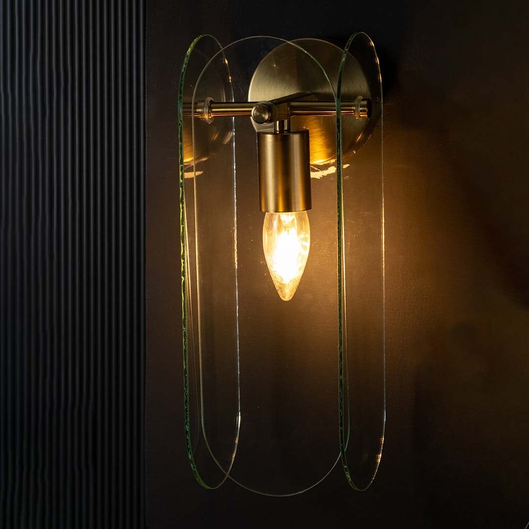 Gold and curved glass wall light glowing warmly on a dark background showcasing its soft ambient glow and elegant layered contemporary design.