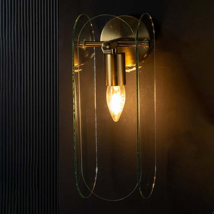 Gold and curved glass wall light glowing warmly on a dark background showcasing its soft ambient glow and elegant layered contemporary design.