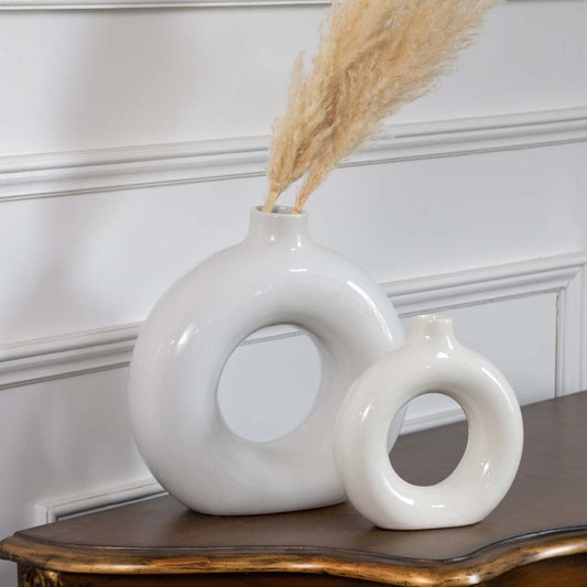 Two glossy white circular vases placed on a wooden table with soft natural decor showing elegant shapes that add a minimal and calming look to the room.