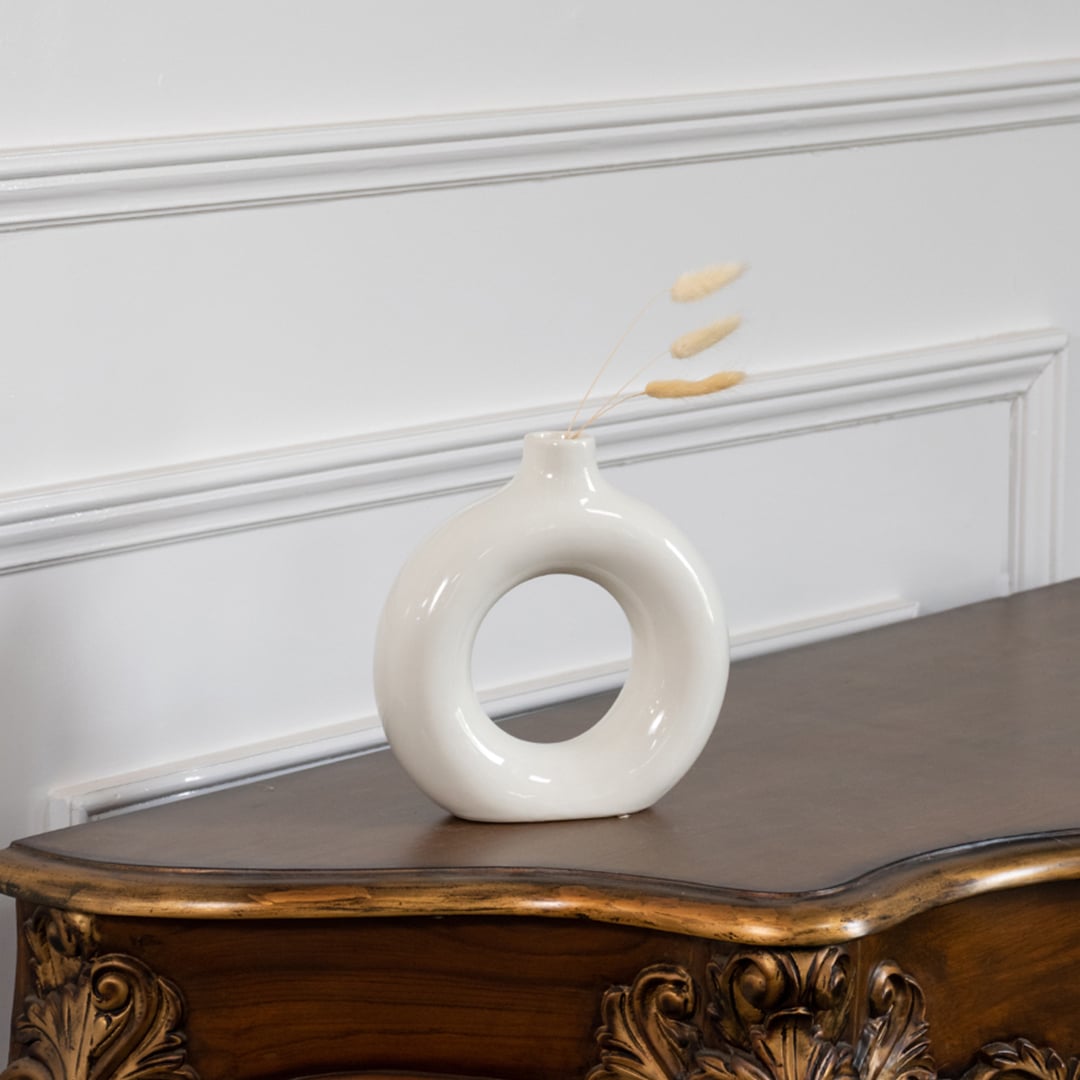 Modern ceramic donut vase in glossy white finish displayed on wooden table with wall paneling elegant lifestyle home decor.