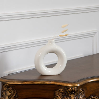 Modern ceramic donut vase in glossy white finish displayed on wooden table with wall paneling elegant lifestyle home decor.