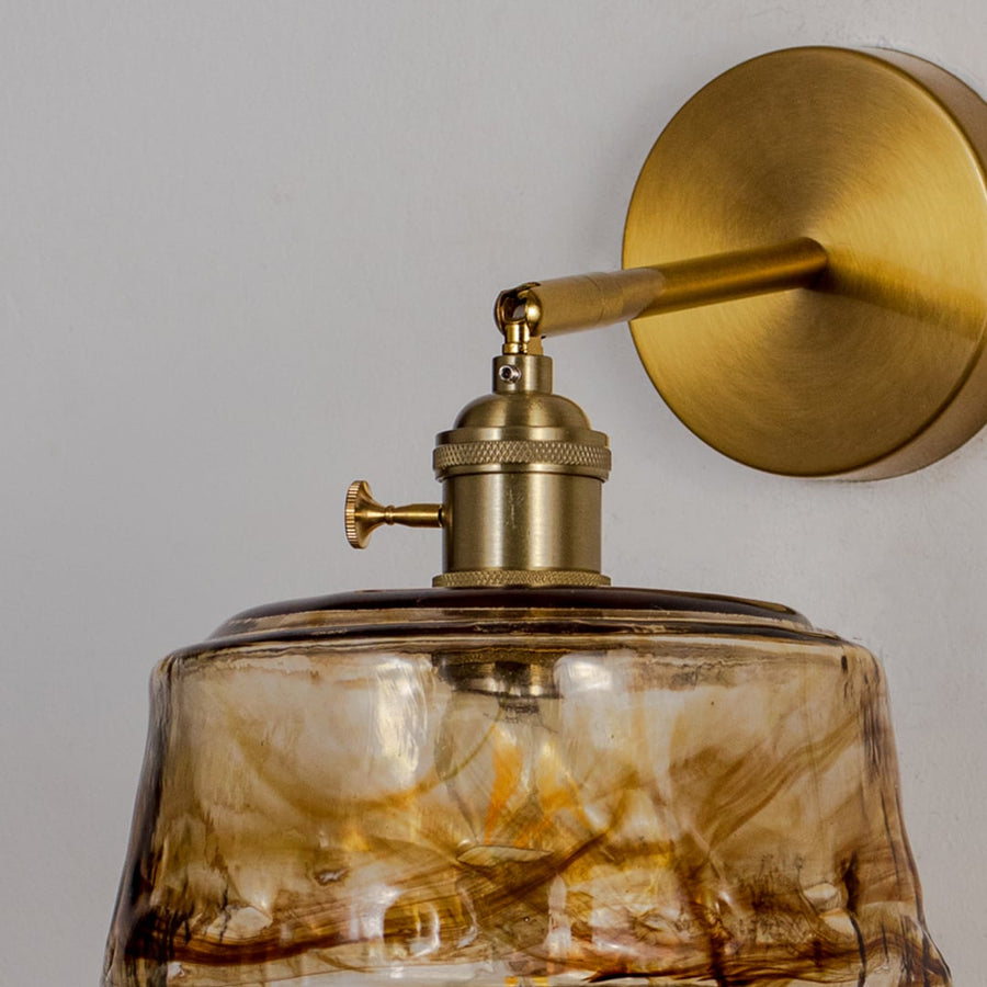 Closeup view of brushed brass wall sconce with amber textured glass shade elegant indoor wall light for home decor.
