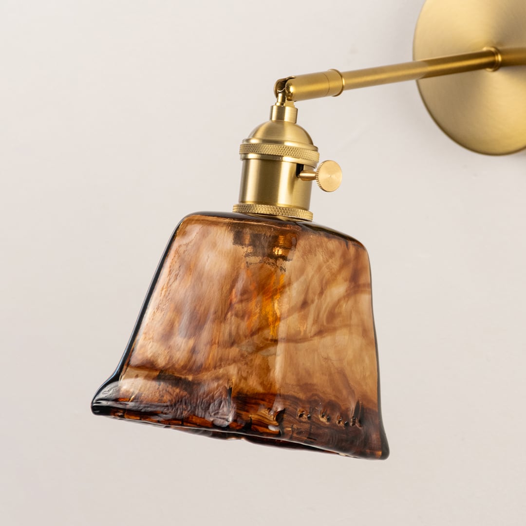 Closeup of brass wall sconce with amber textured glass shade premium indoor wall light for bedroom and hallway lighting decor.
