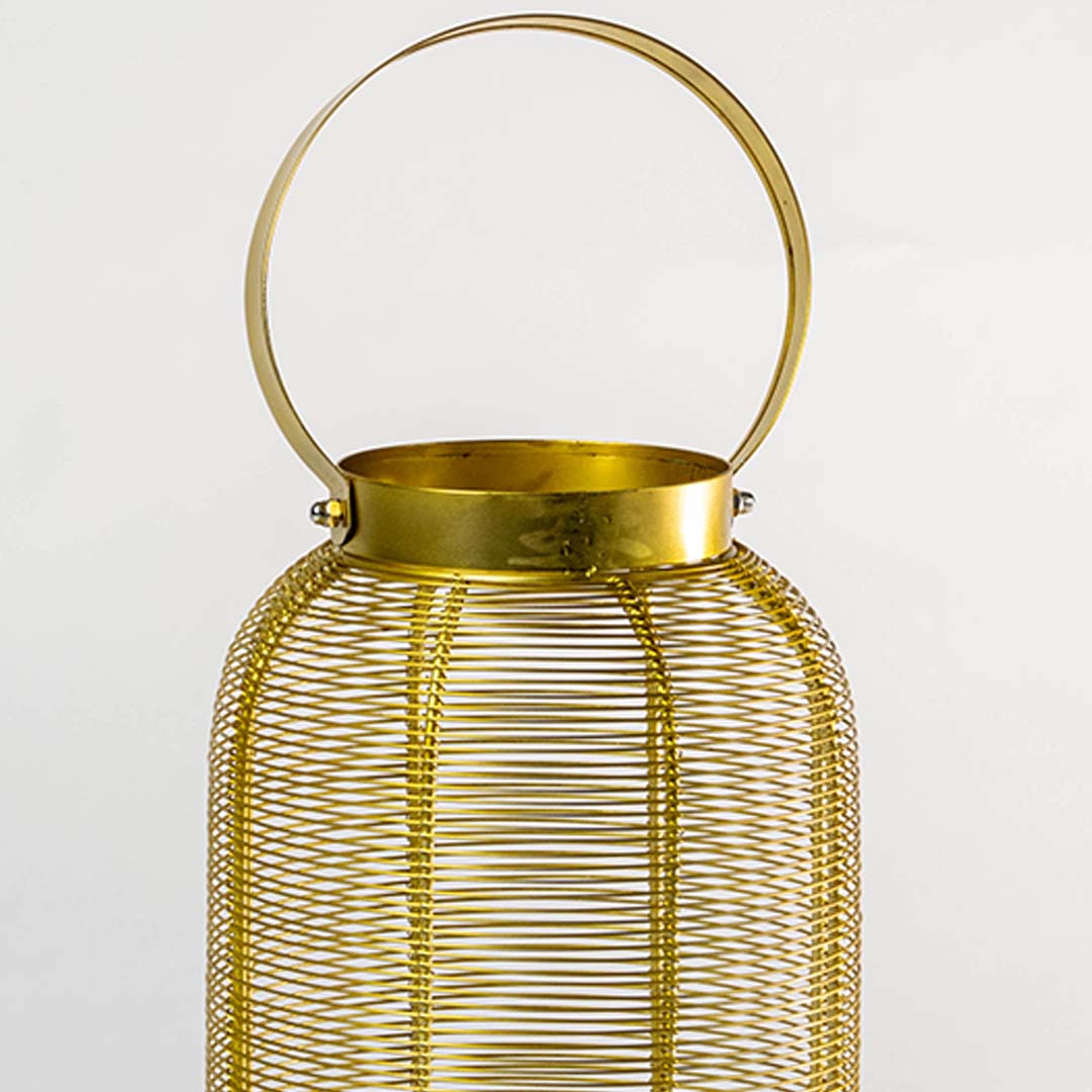 Closeup view of gold metal wire mesh texture and circular handle detail on decorative candle lantern with warm metallic finish.