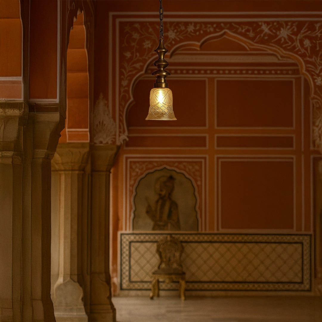 Antique brass pendant light with etched glass shade hanging in a traditional Jaipur palace hallway with red walls and arches.