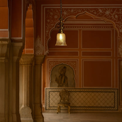 Antique brass pendant light with etched glass shade hanging in a traditional Jaipur palace hallway with red walls and arches.