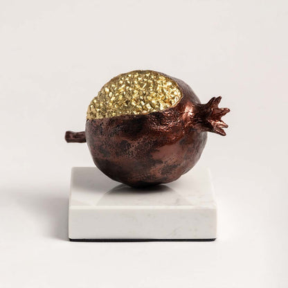 Golden pomegranate sculpture on marble base displayed against clean white background for a minimalist view.